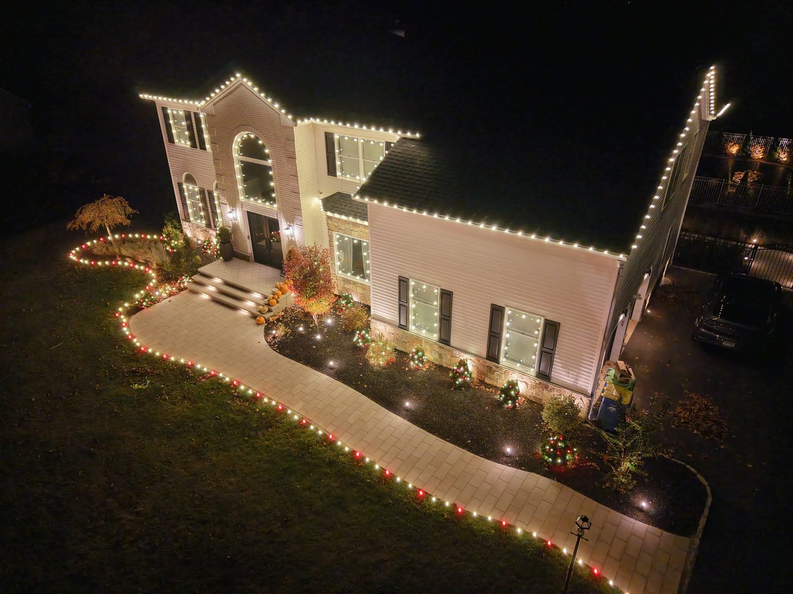 A lit walkway curving to a decorated house, the path edged in warm bulbs