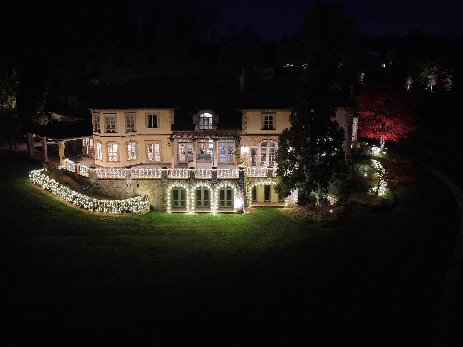 A large home with its facade lit and roofline outlined, seen across the lawn at night