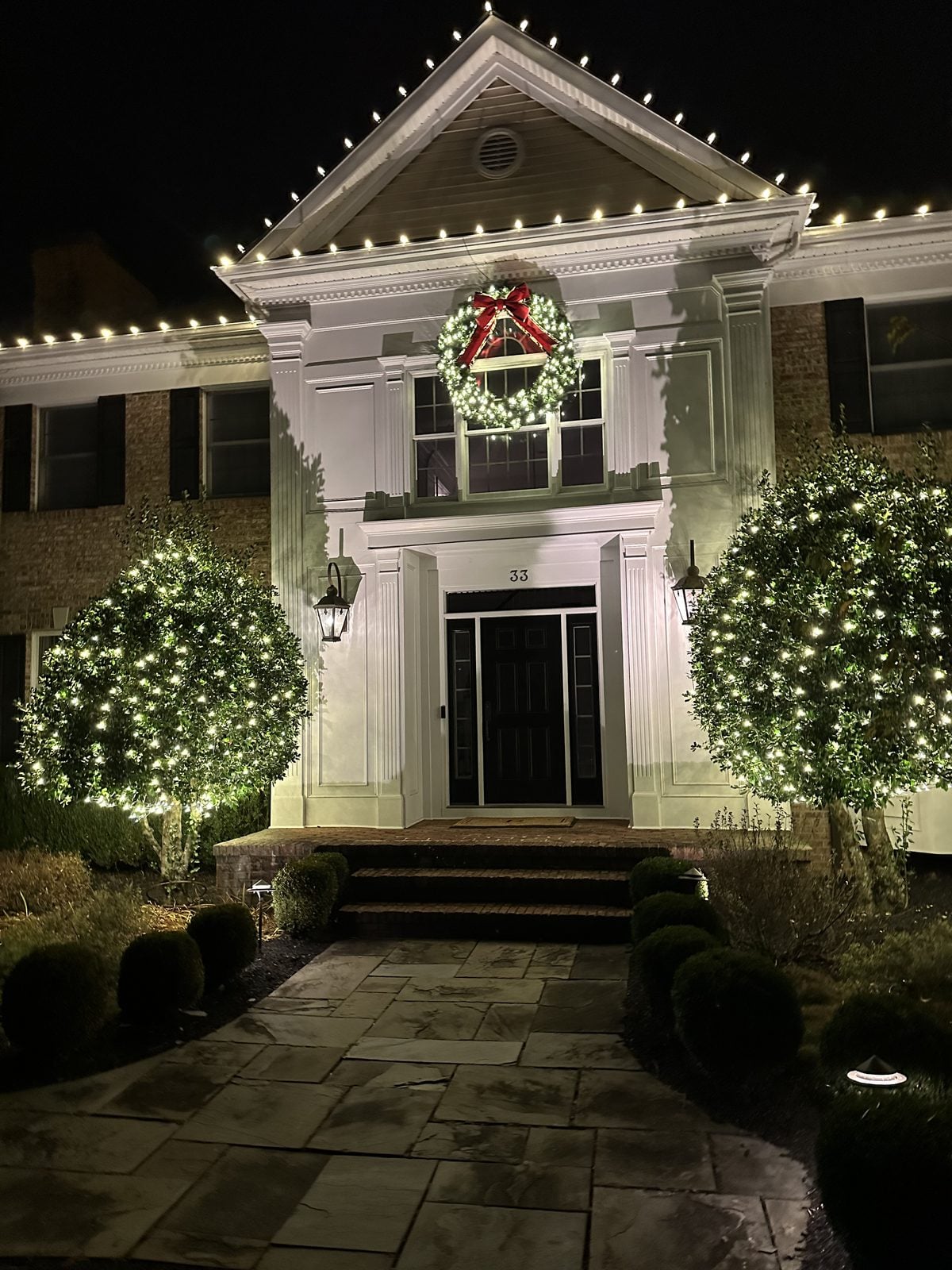A pedimented entry with a lit wreath above the door and decorated evergreens either side
