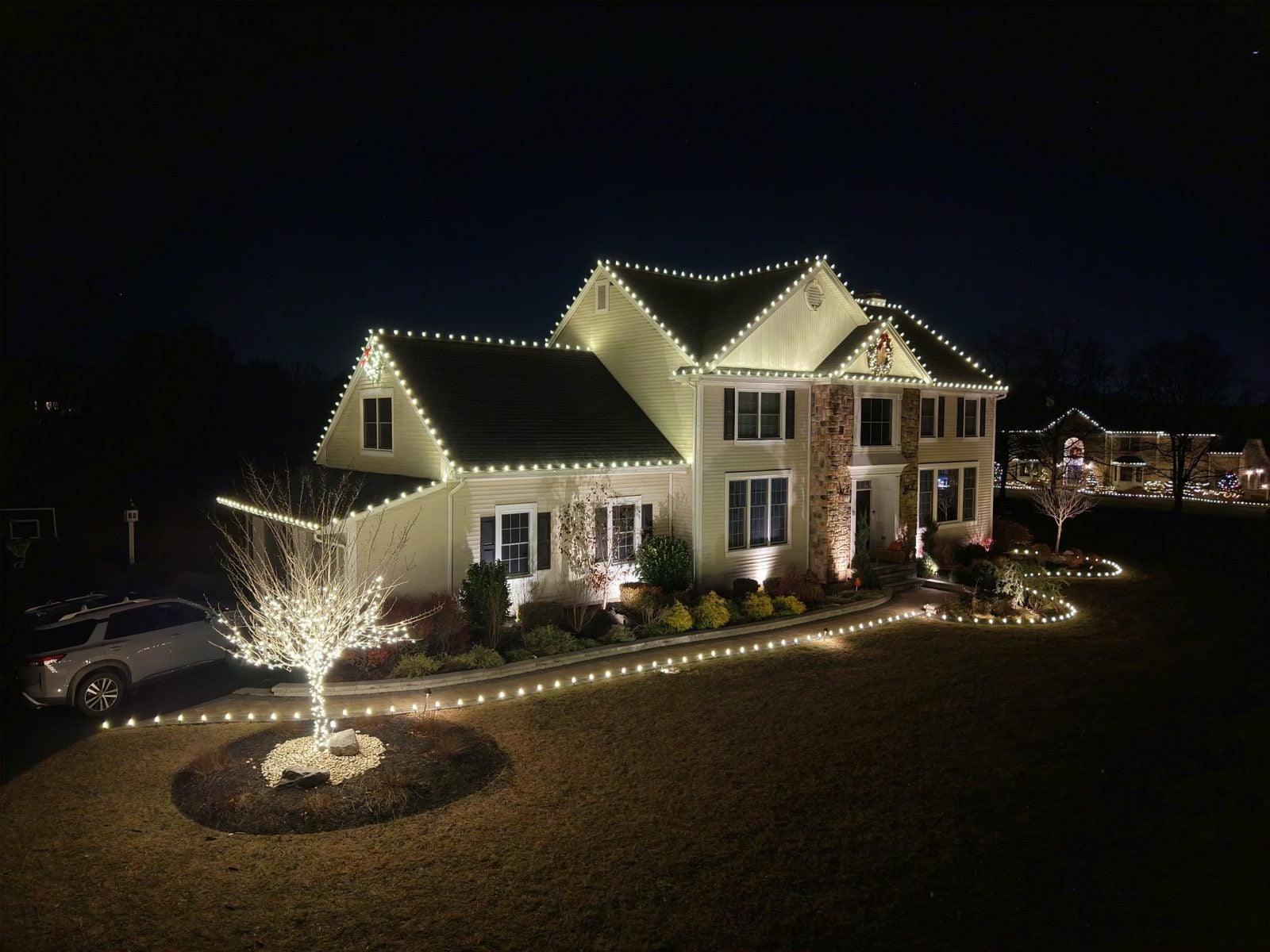 A house outlined in warm bulbs with the front path and specimen trees lit to match