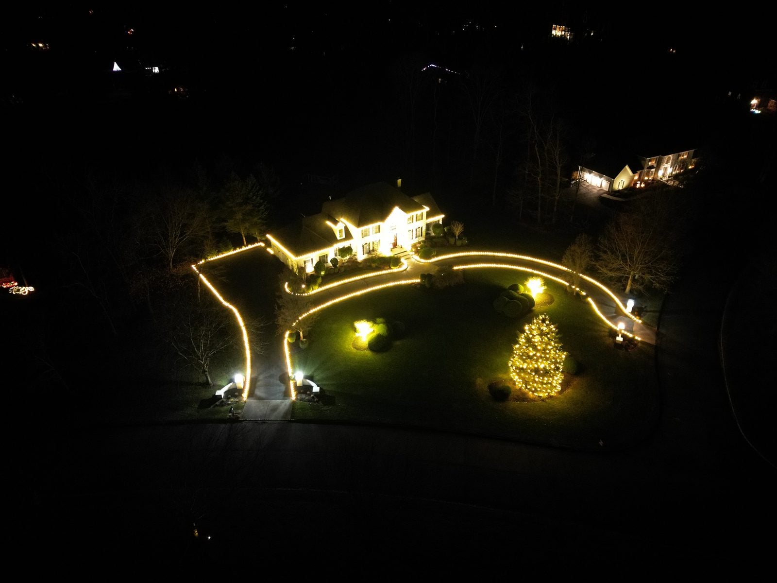 An aerial view of a decorated property, the drive outlined in light around a lit tree