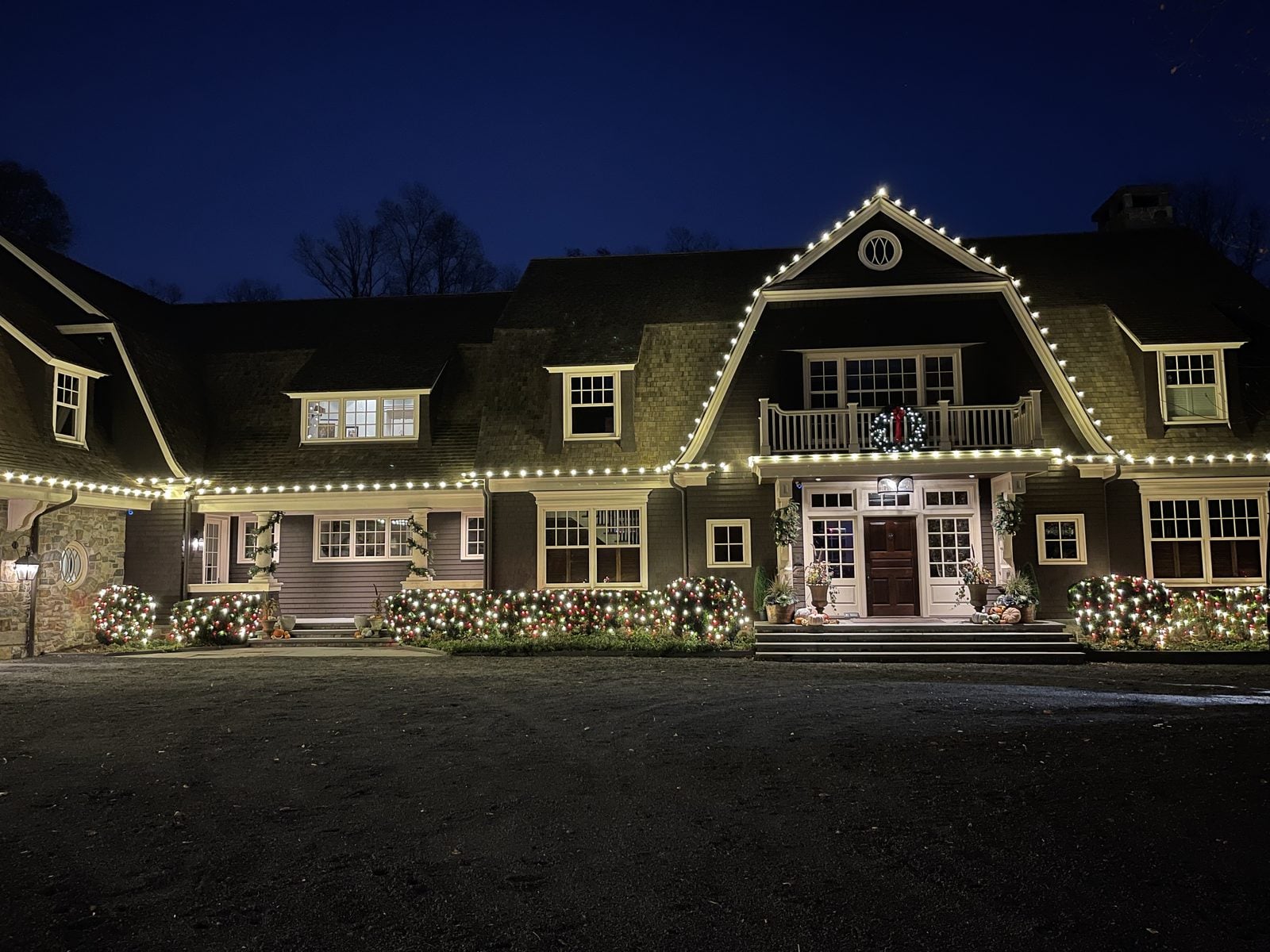 A gambrel-roofed house with warm bulbs following every roof line