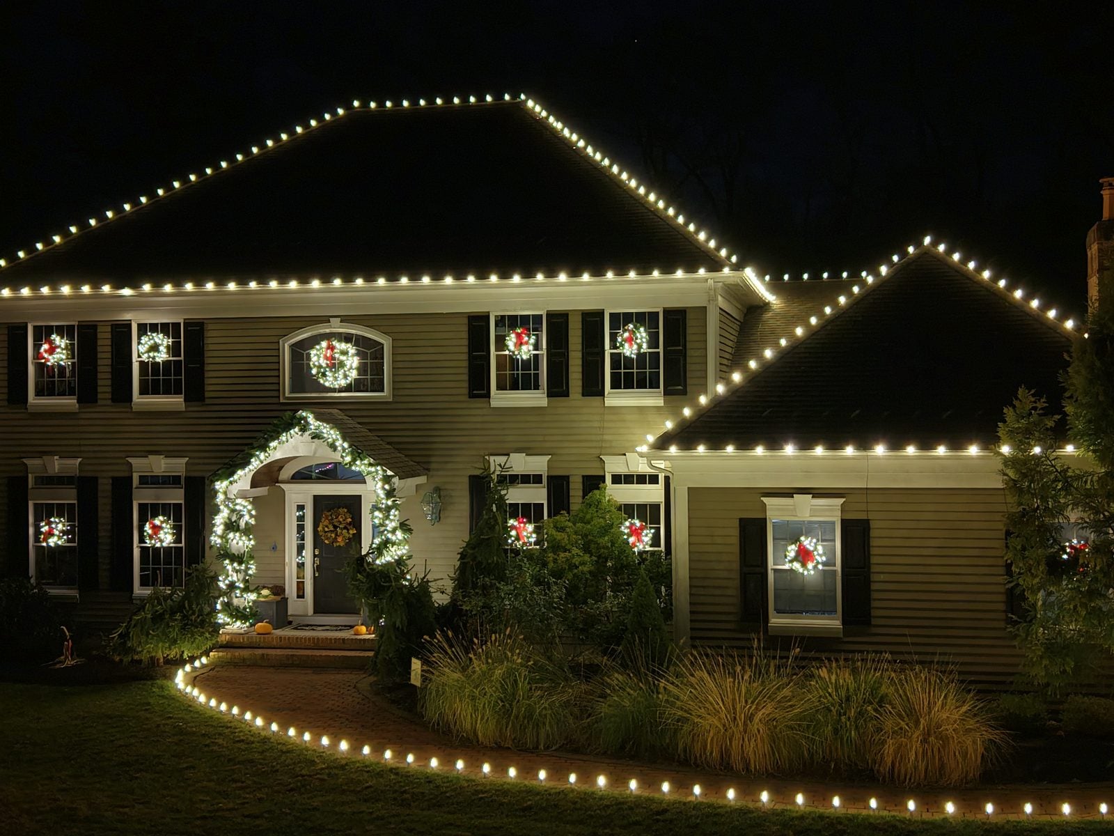 A house outlined in bulbs with lit wreaths on the windows and the walkway edged in light