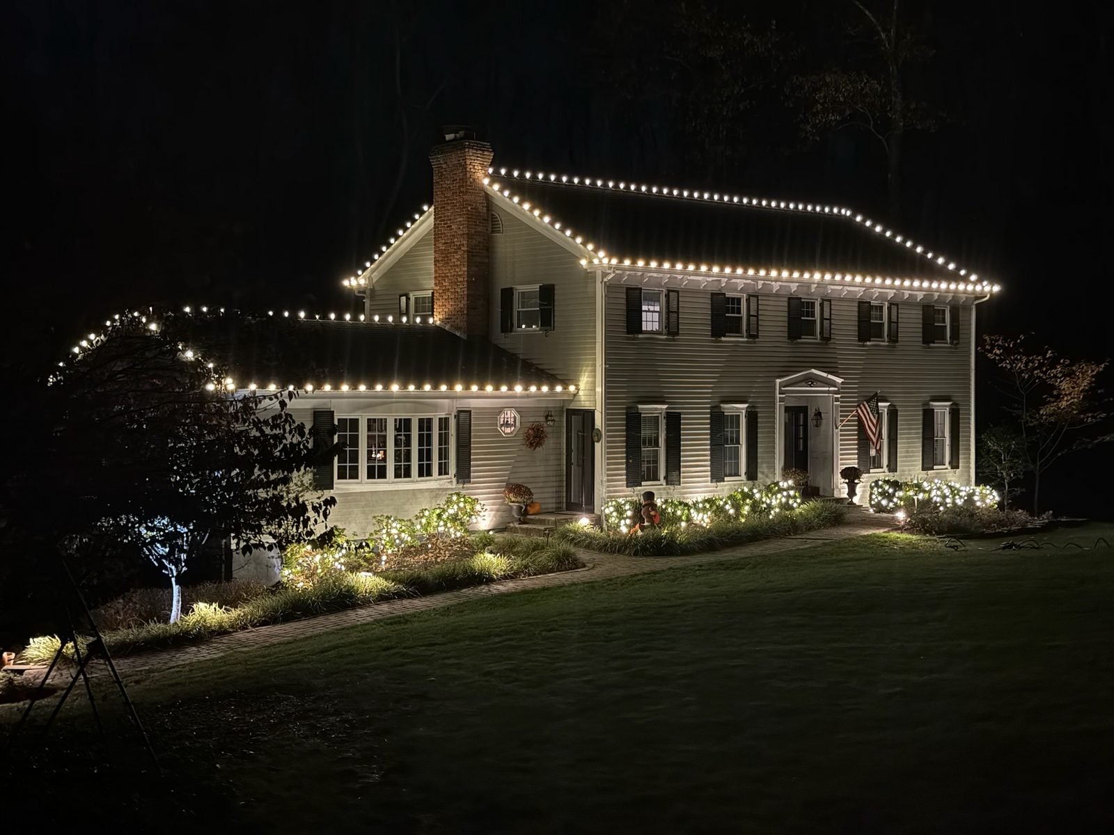 A white colonial outlined in warm bulbs, garland and wreaths across the front