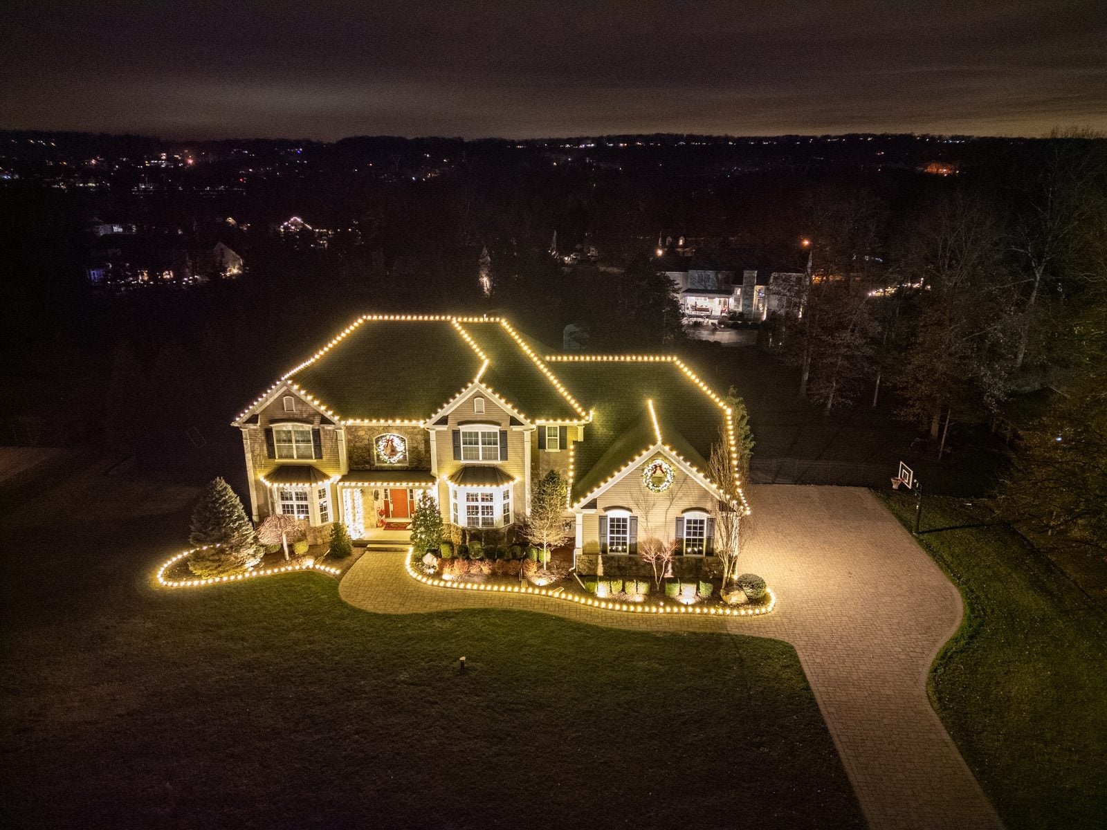 An aerial view of a lit home at night, the driveway traced in warm light