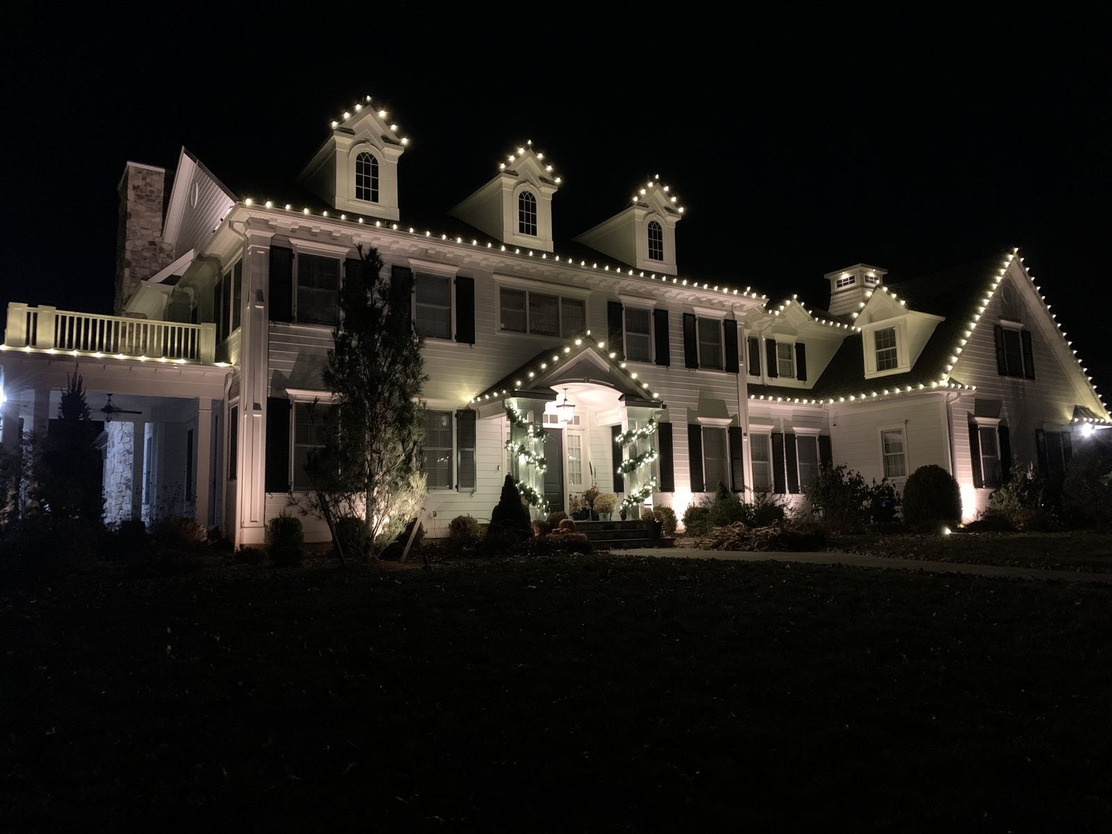 A large home with warm bulbs along the eaves and dormers at night