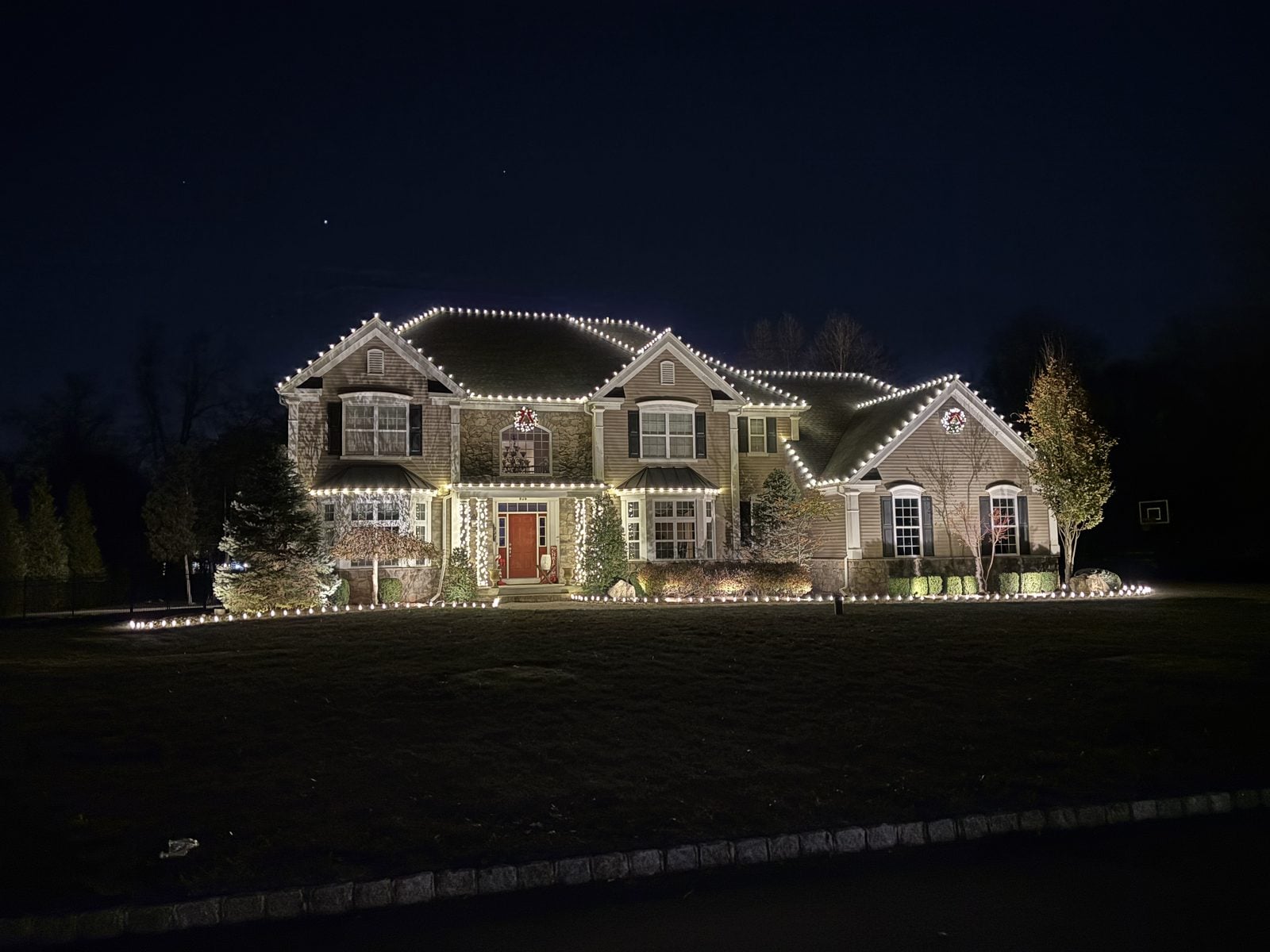 A house outlined in warm bulbs across a dark lawn