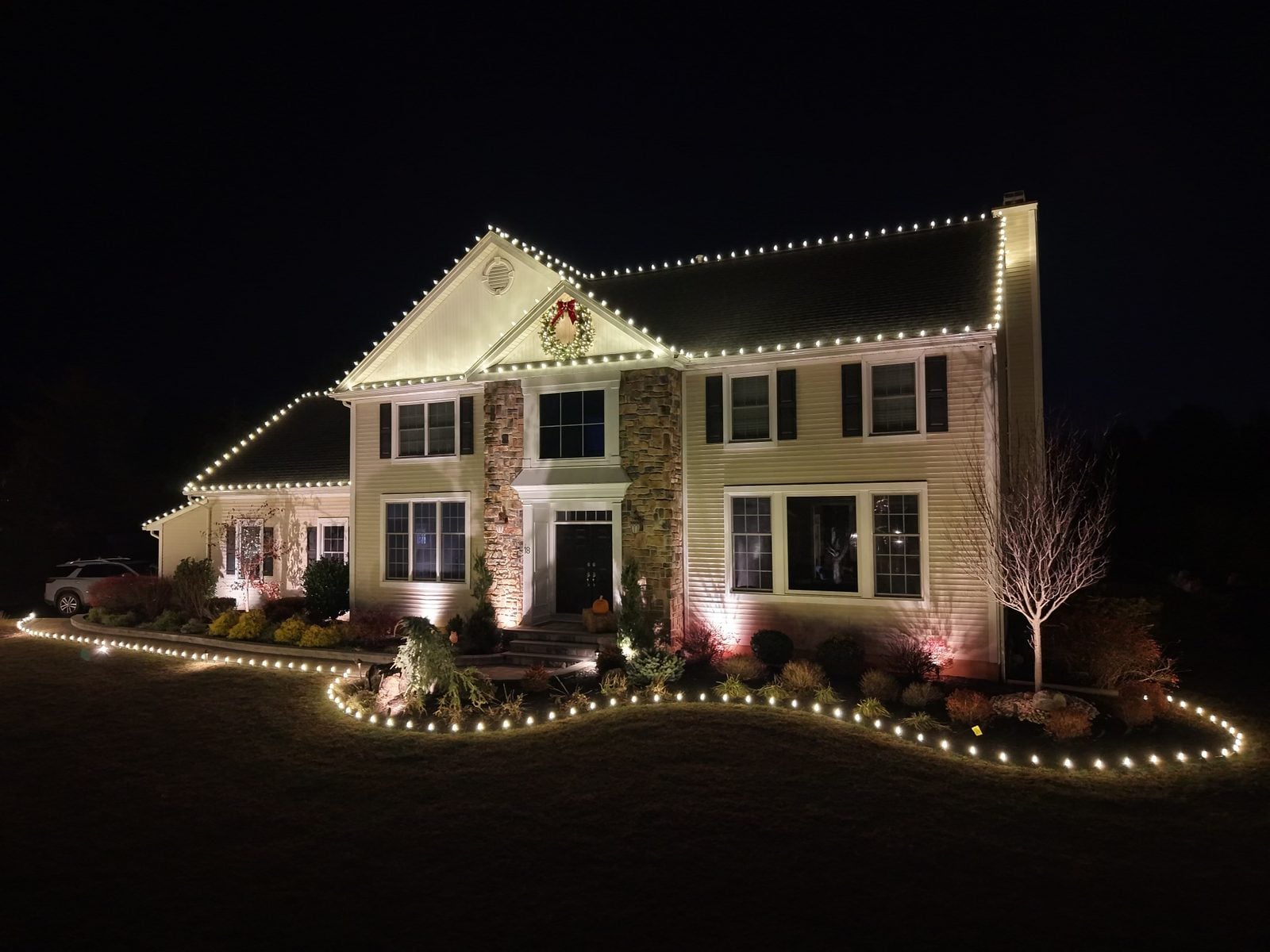 A decorated house with its roofline in warm bulbs and coloured uplights in the beds