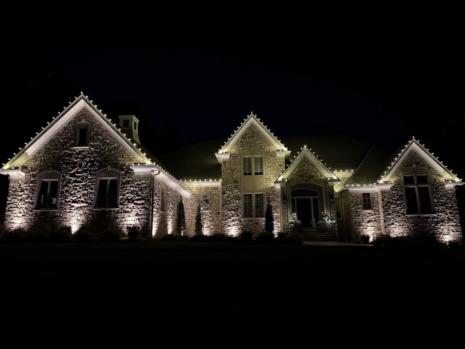 A stone-fronted house outlined in warm bulbs at night