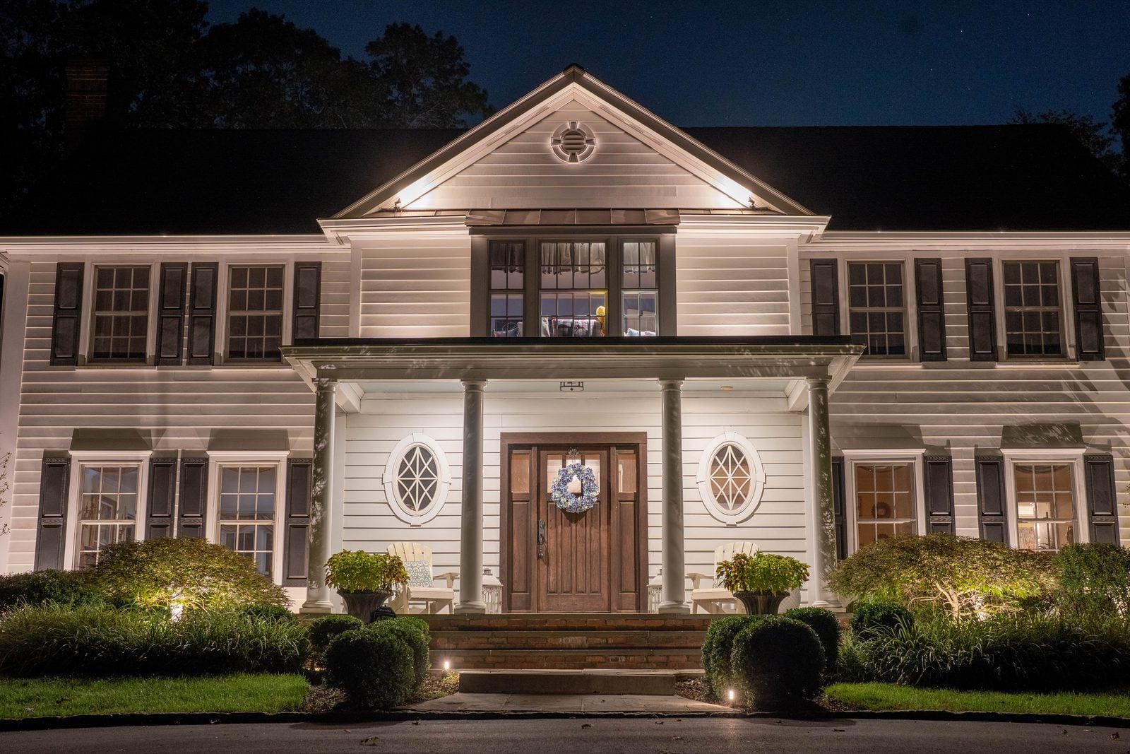 The symmetrical front elevation of a white colonial, columns and pediment grazed with warm light