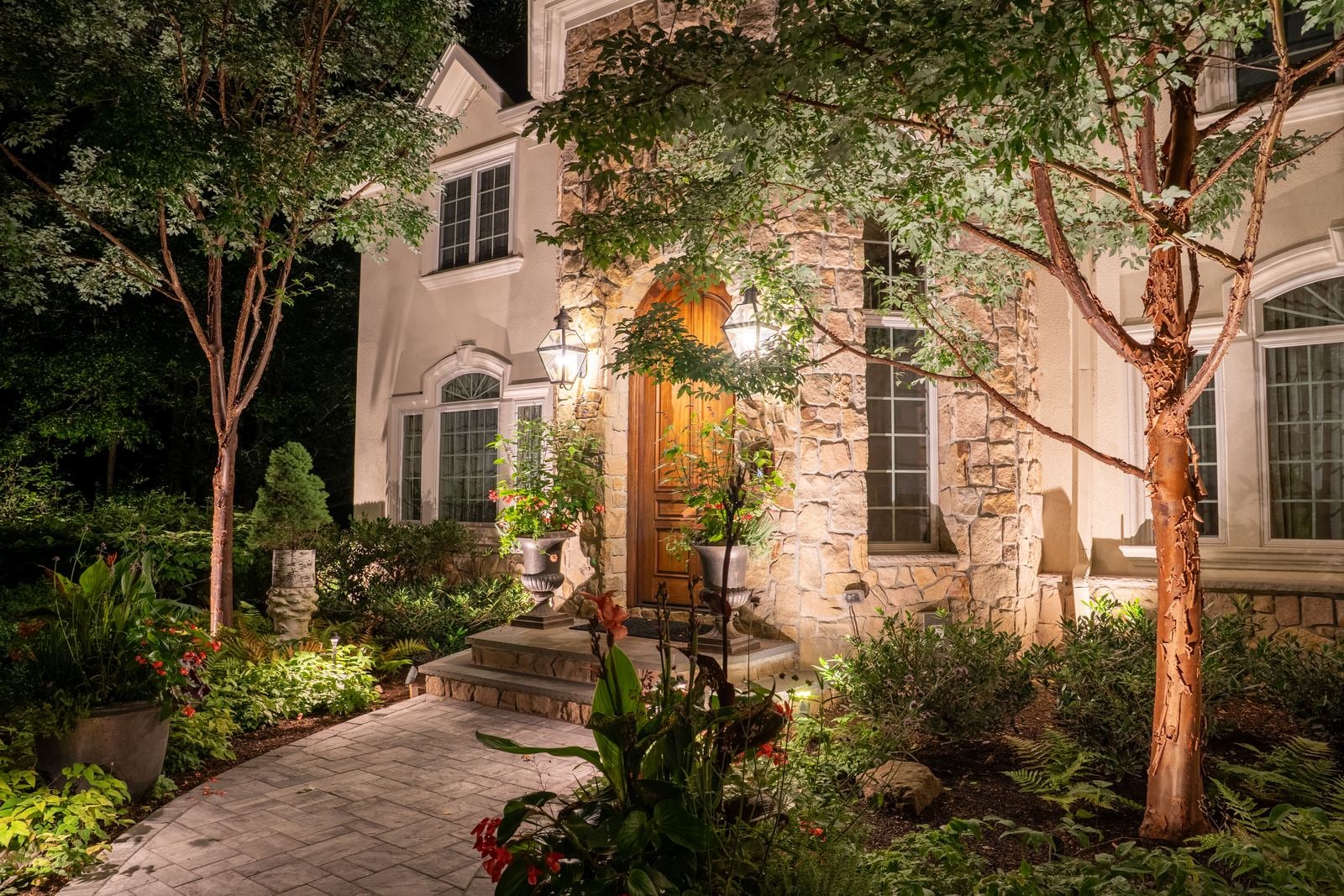 A stone entry framed by an uplit tree, the walk lit to the door