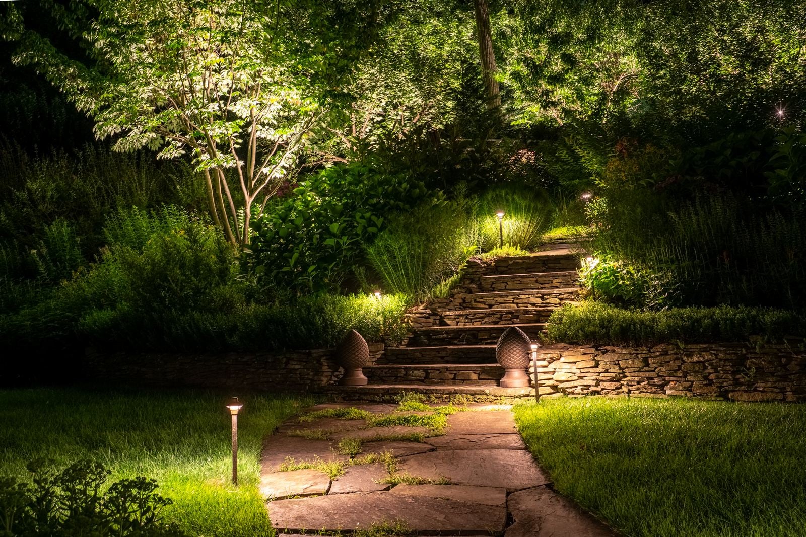 A lit garden route at blue hour, planting layered in warm light