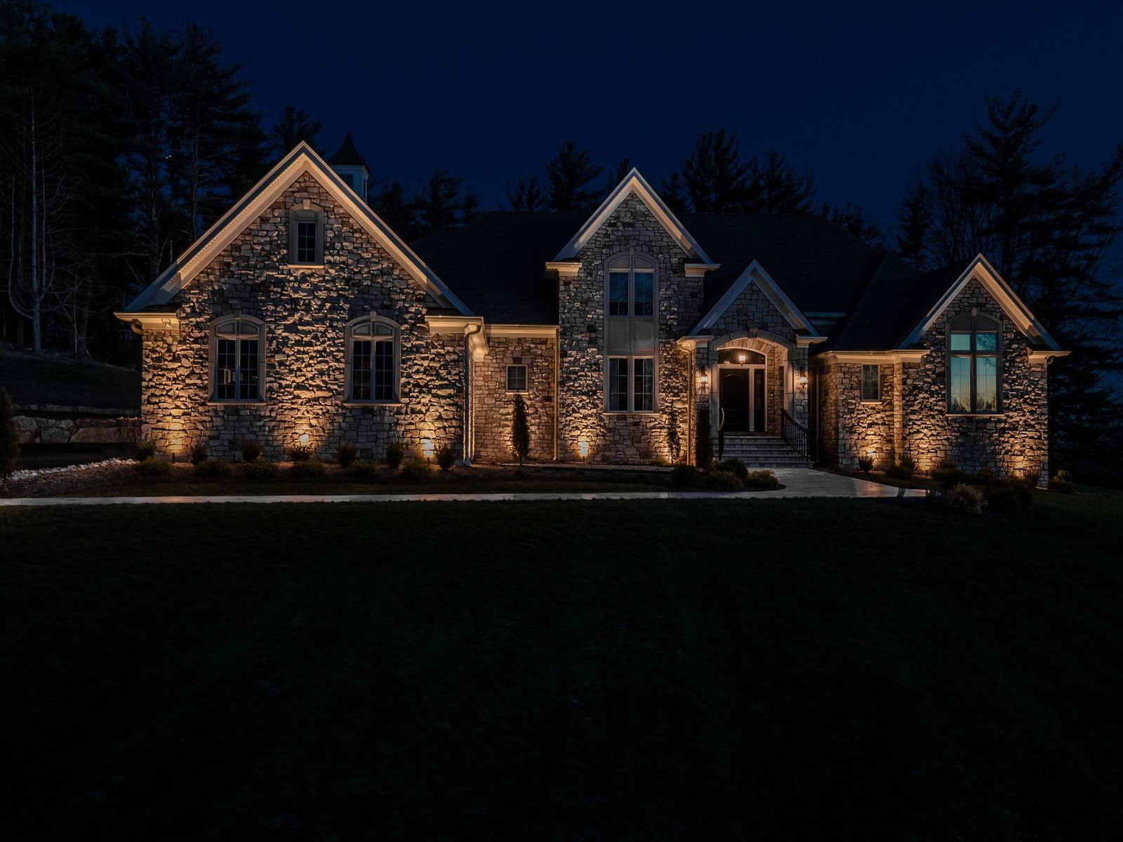 A lit home elevation at blue hour, planting beds washed from below