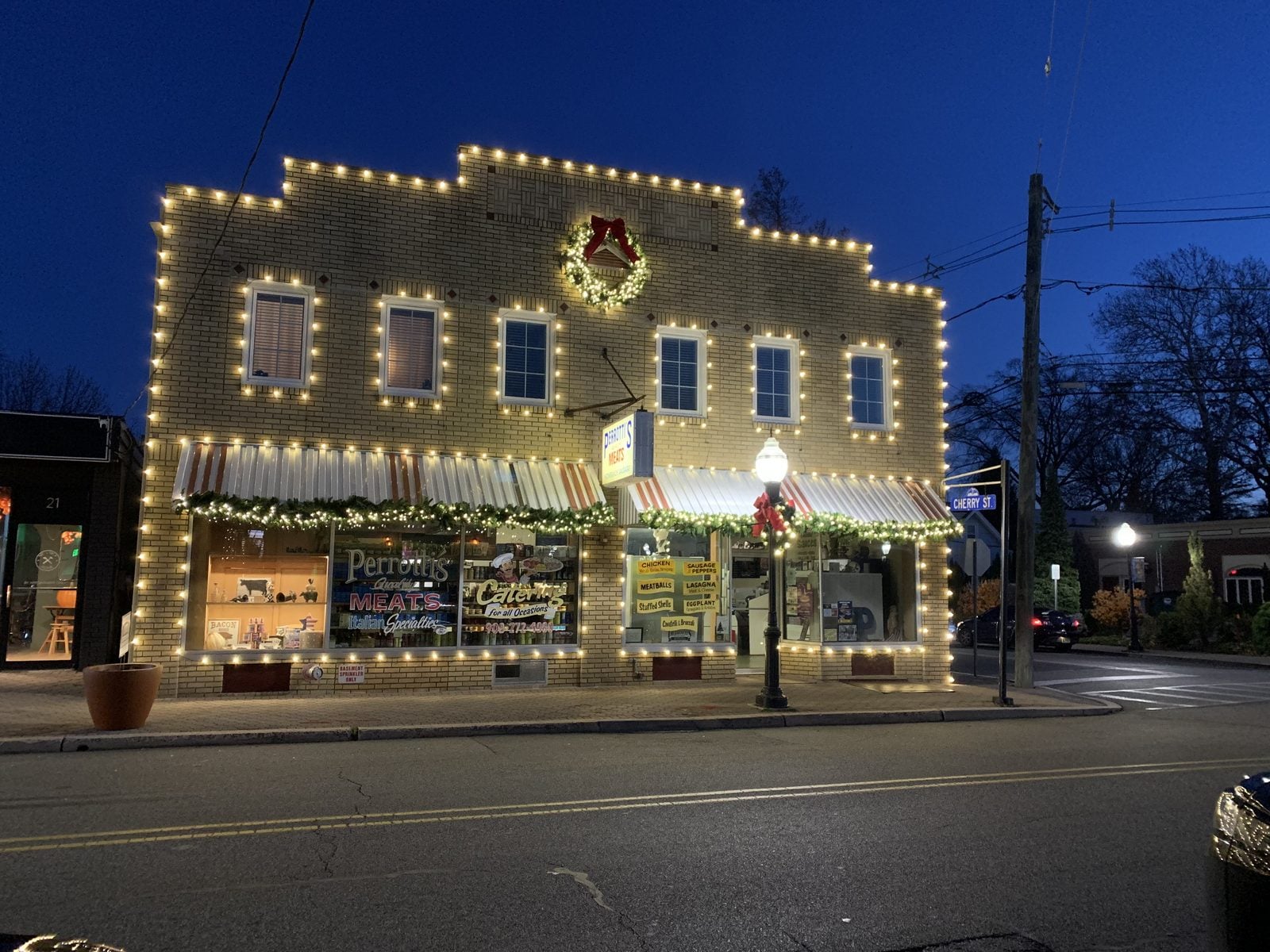 A storefront on a main street at blue hour, its windows and roofline picked out in bulbs
