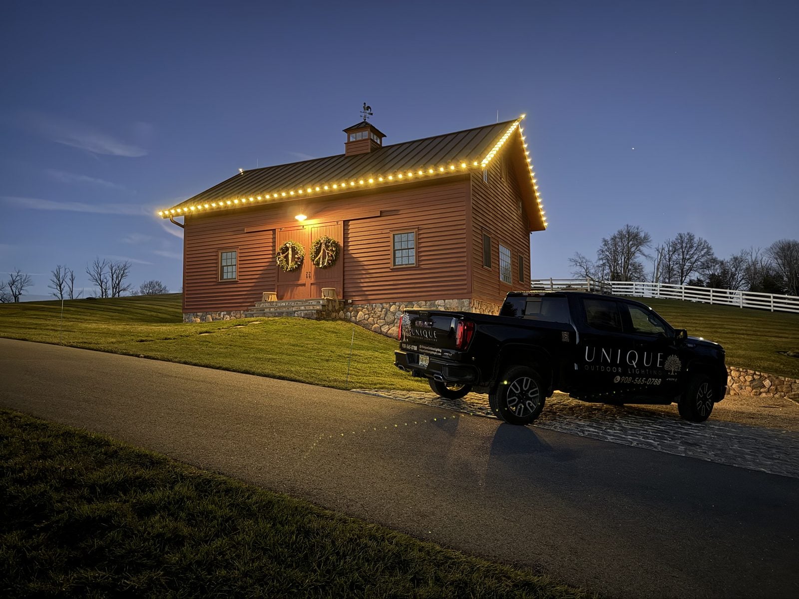 A red barn with a warm-lit roofline and wreaths on the doors