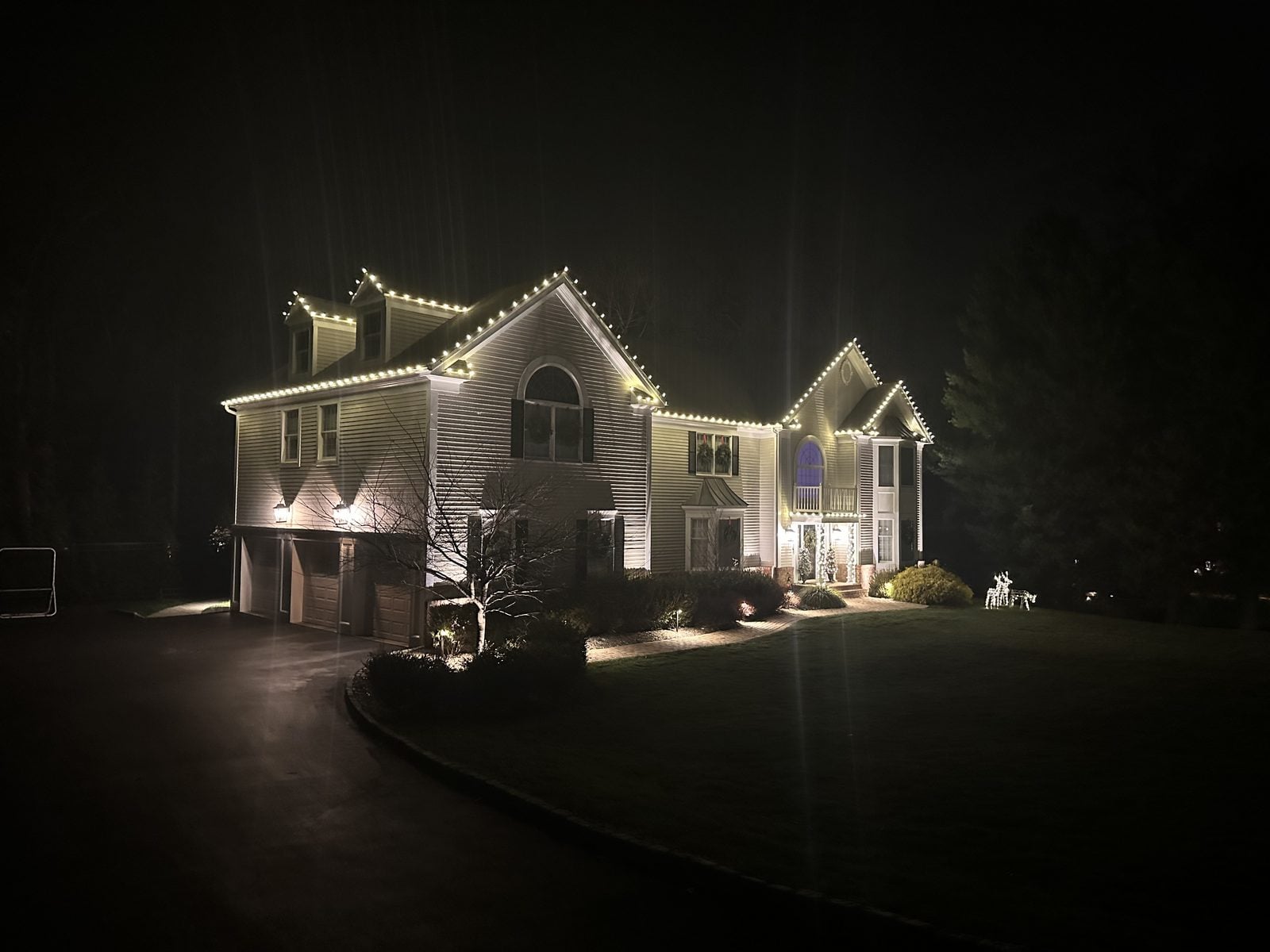 A decorated home seen from the driveway, roofline and entry lit