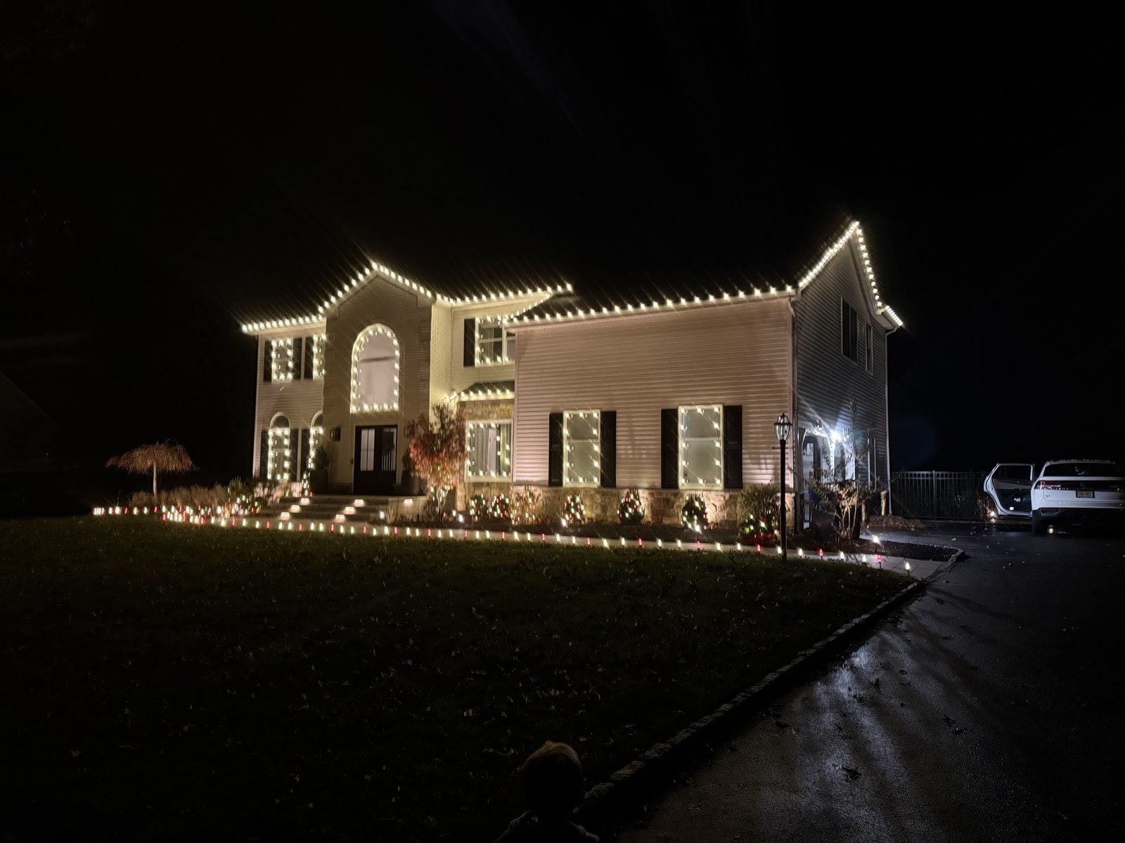 A house outlined in warm bulbs with the front walk lit to the door