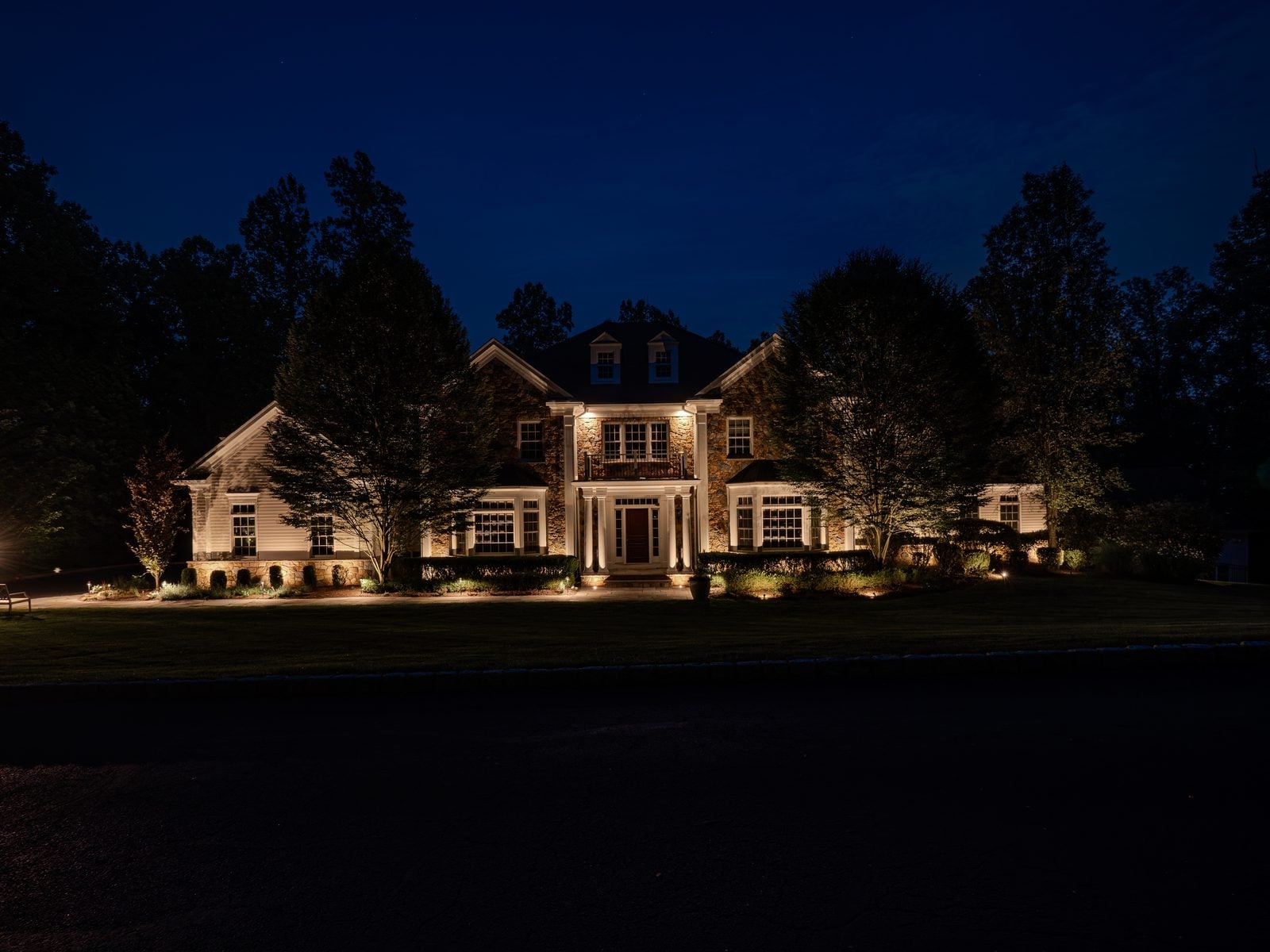 A colonial home at deep blue hour with every gable and dormer picked out in warm light