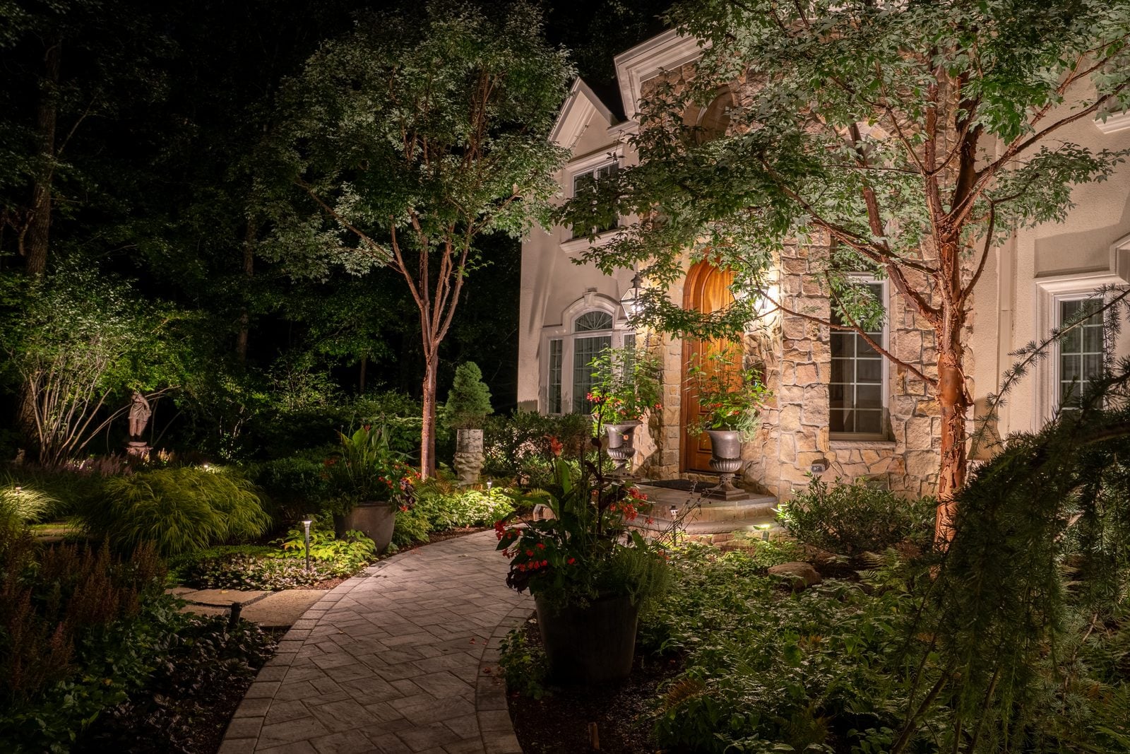 A lit walkway curving through planting toward a warm front door