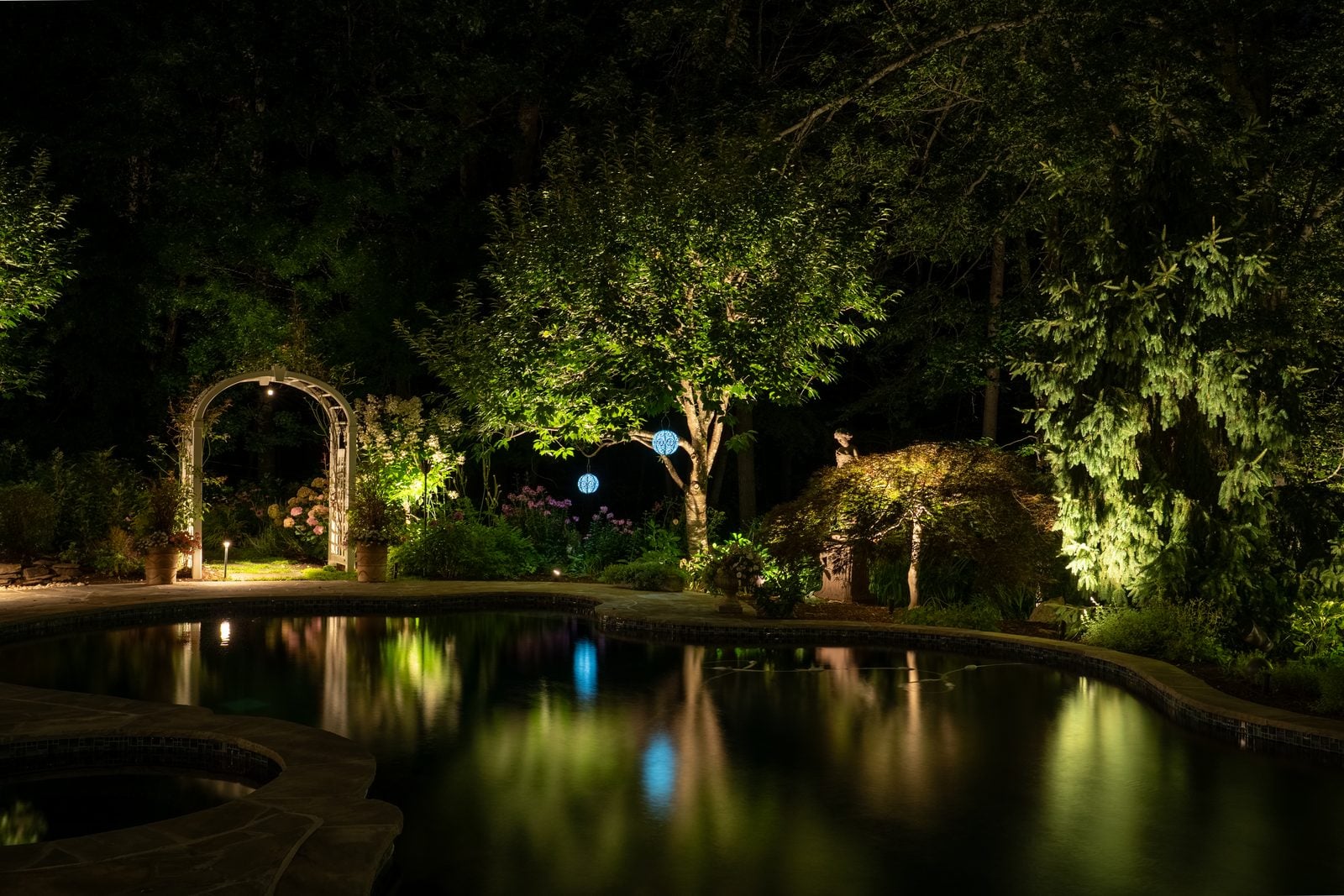 Specimen trees uplit through their canopies above a lit walk