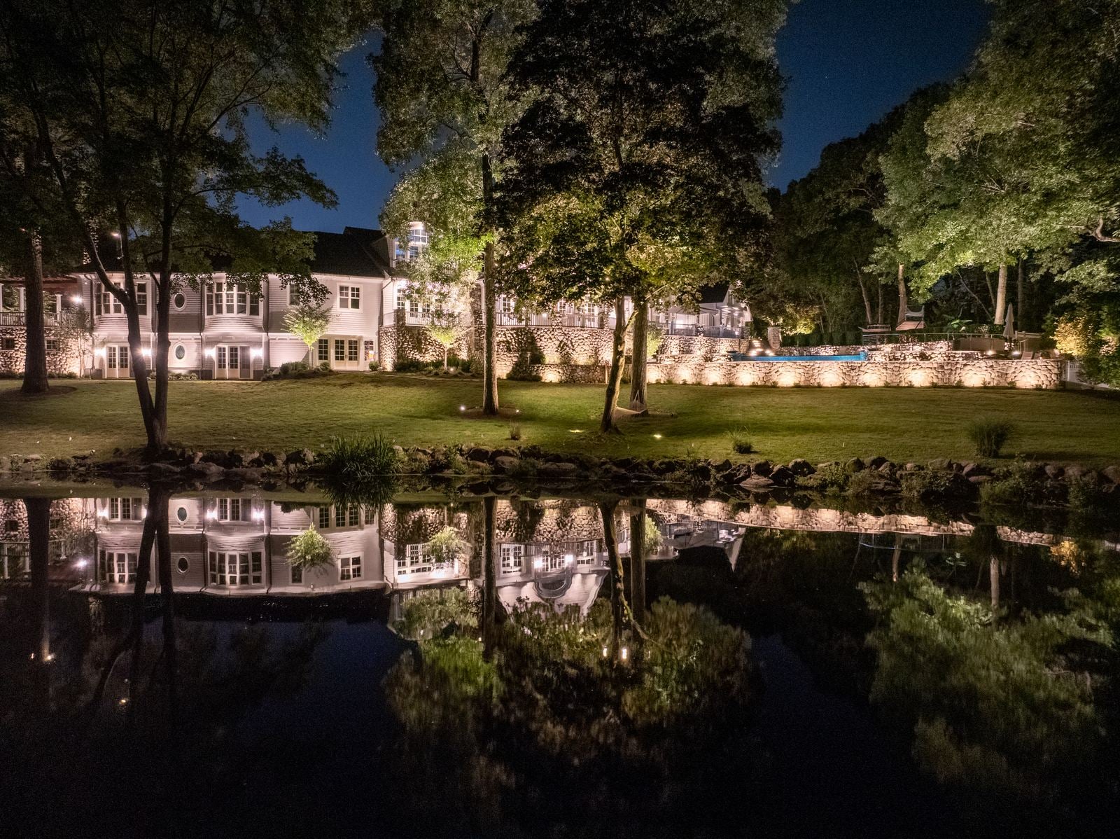 A lit pool at night, the water glowing beneath warm light on the surrounding planting