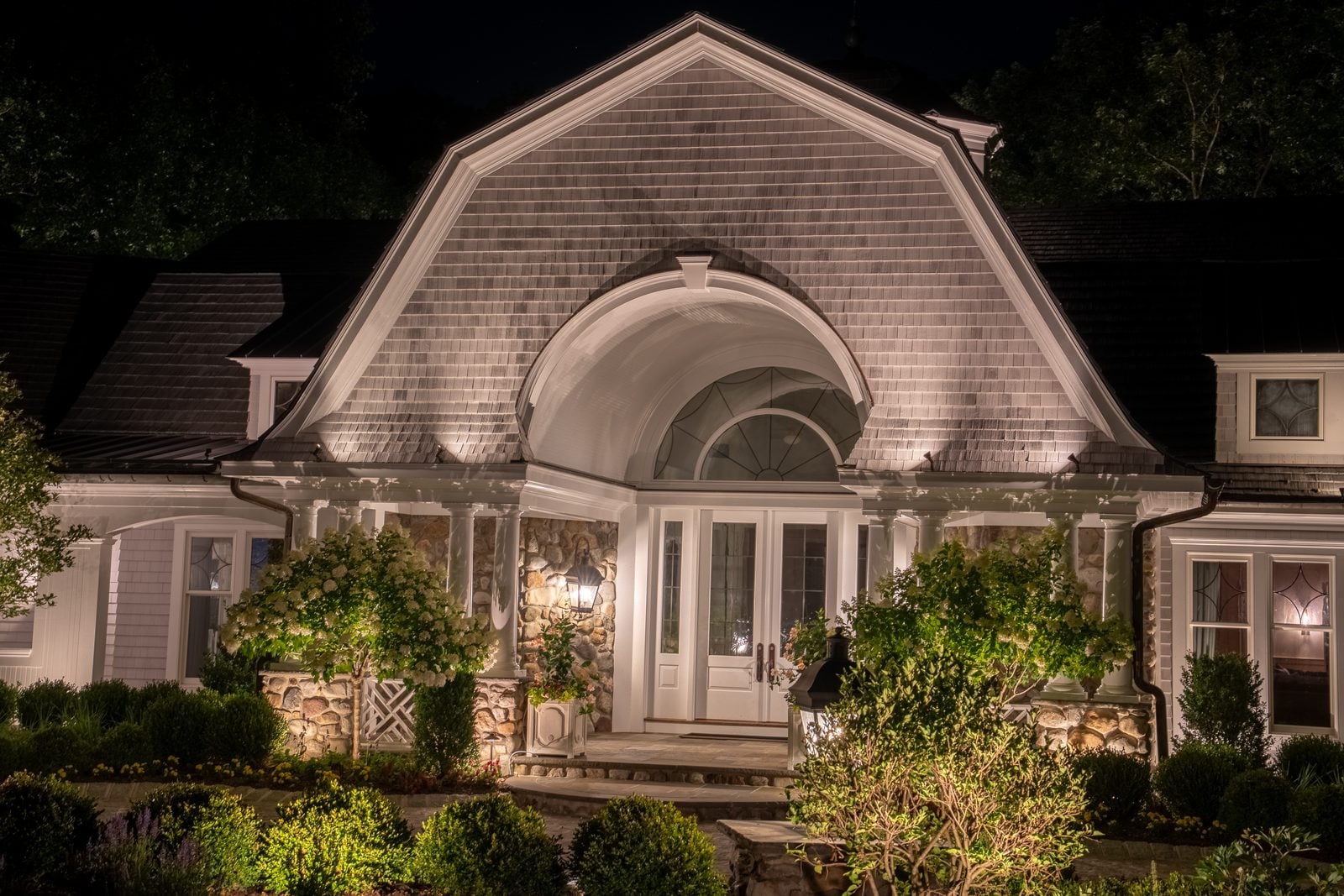 A lit home elevation at blue hour, planting beds washed from below