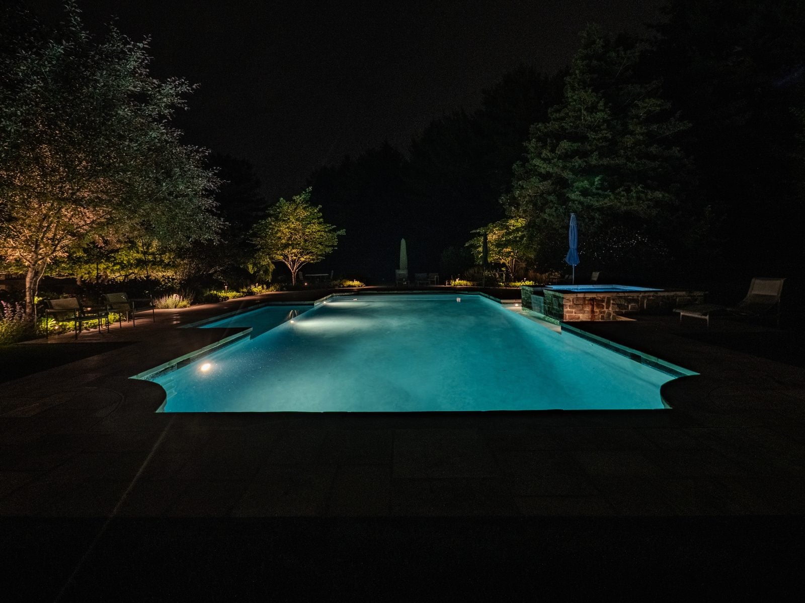 A lit pool at night, the water glowing beneath warm light on the surrounding planting