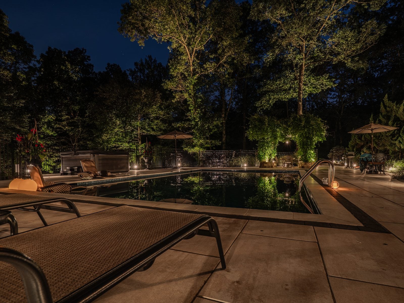 A pool and terrace lit after dark, the far planting uplit above the waterline
