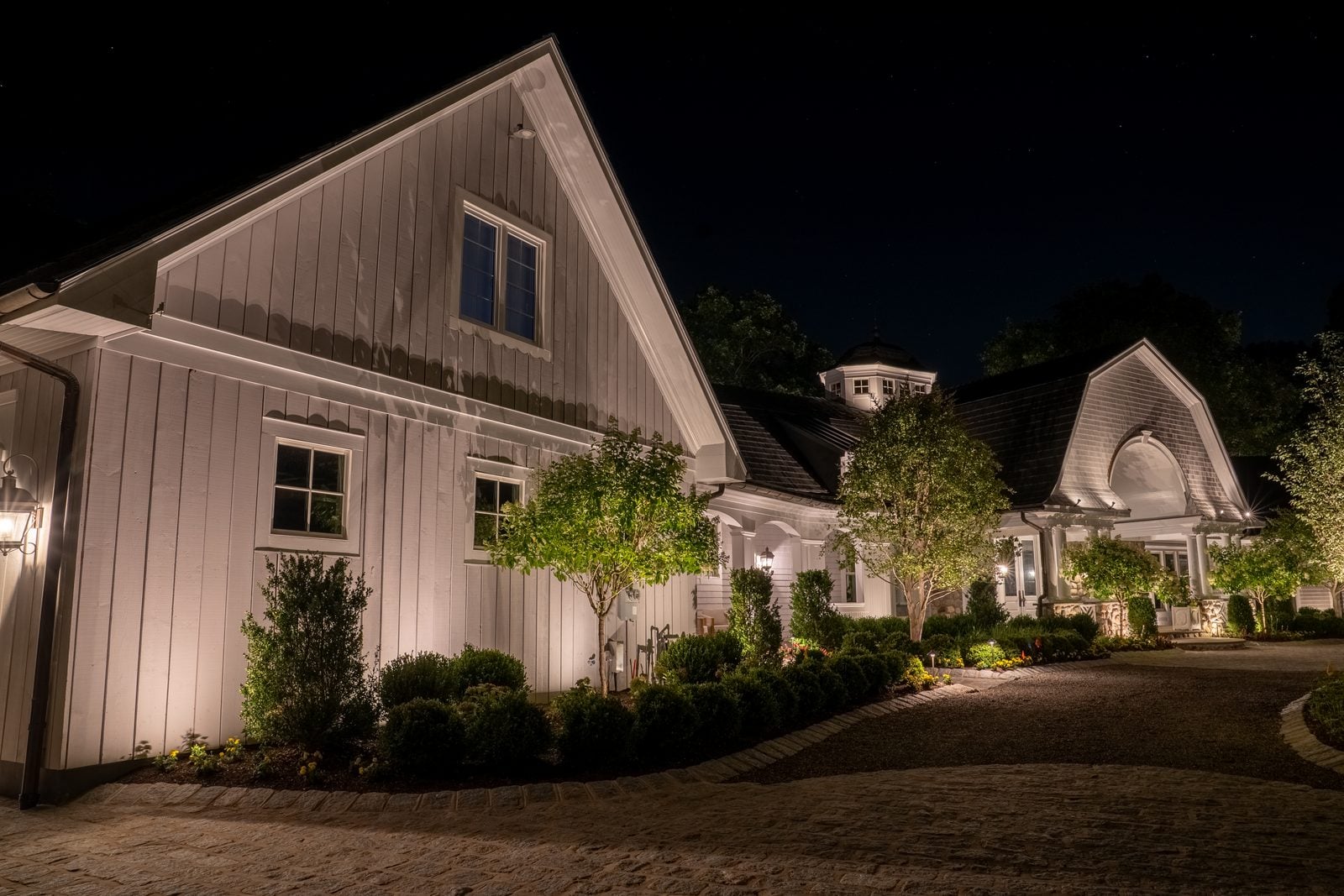 An entry and facade lit from the ground, the drive reading clearly up to the door