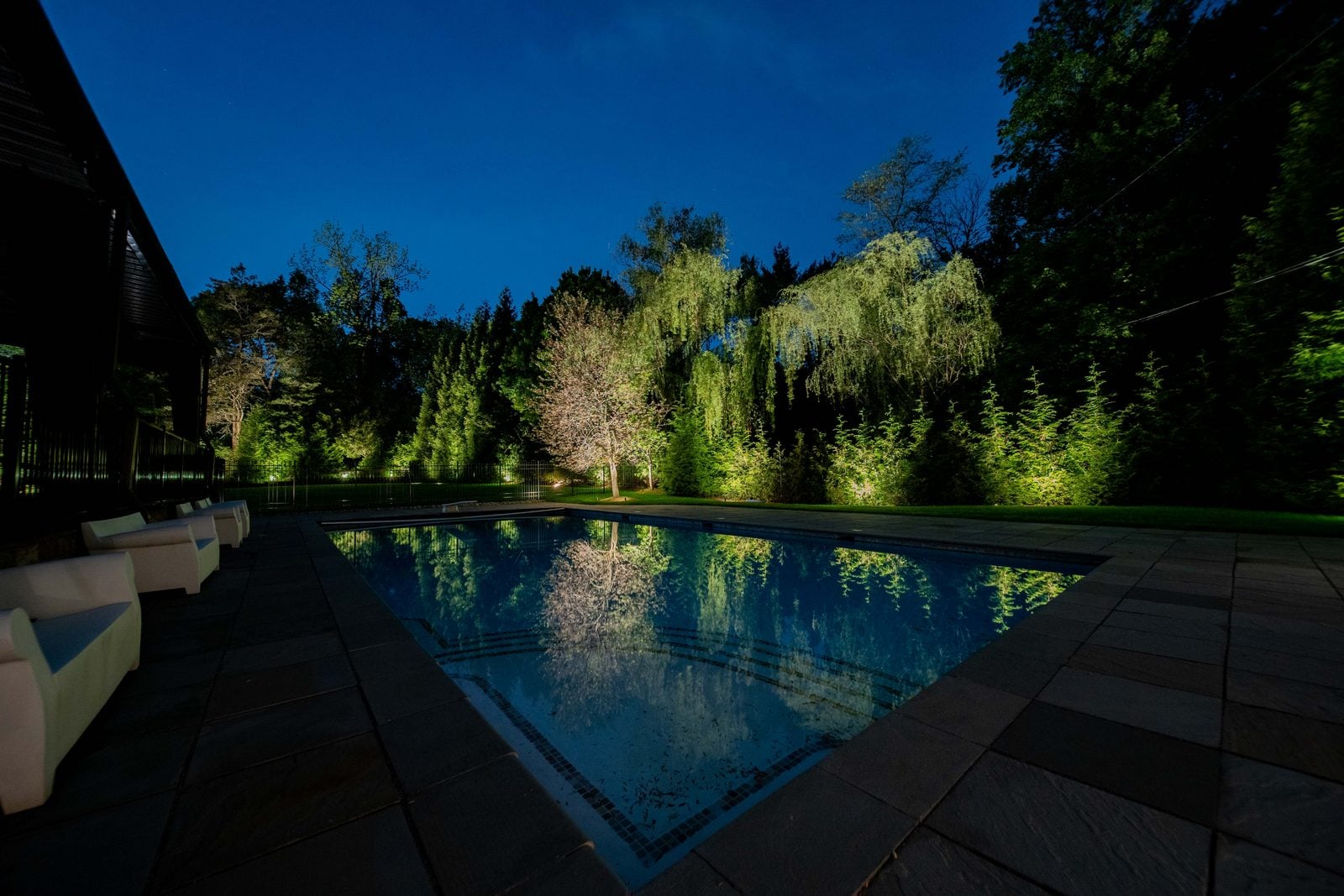 A lit pool at night, the water glowing beneath warm light on the surrounding planting