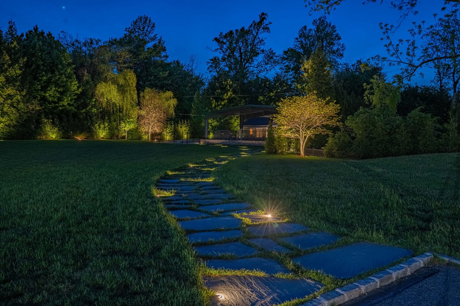 A lit garden route at blue hour, planting layered in warm light