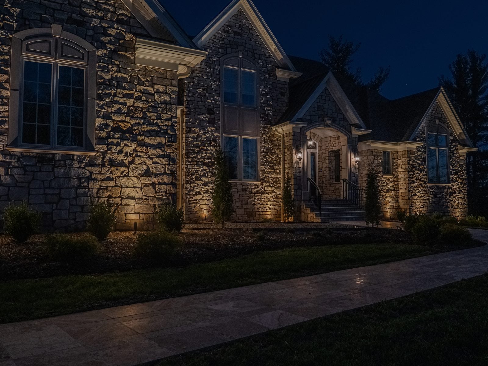 An entry and facade lit from the ground, the drive reading clearly up to the door
