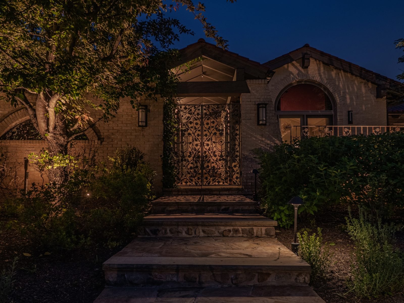 A lit home elevation at blue hour, planting beds washed from below