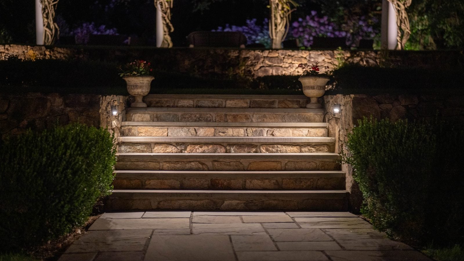 Stone steps between two urns, each tread lit from the wall beside it