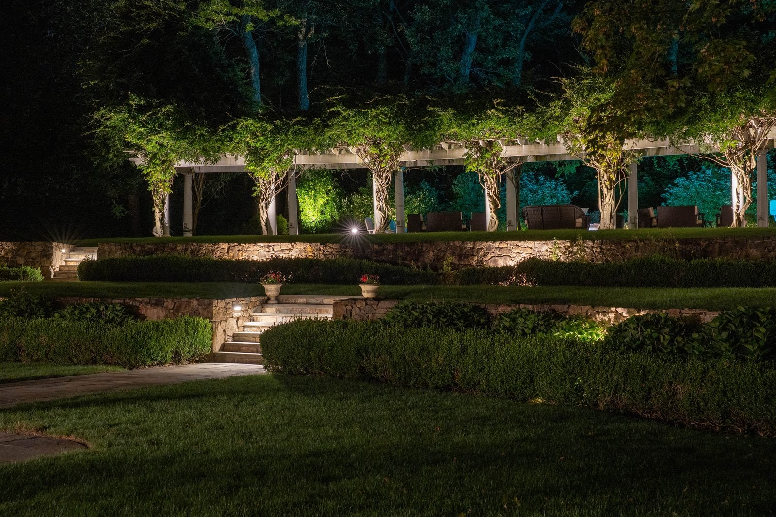 A long pergola arcade lit column by column above a stone terrace