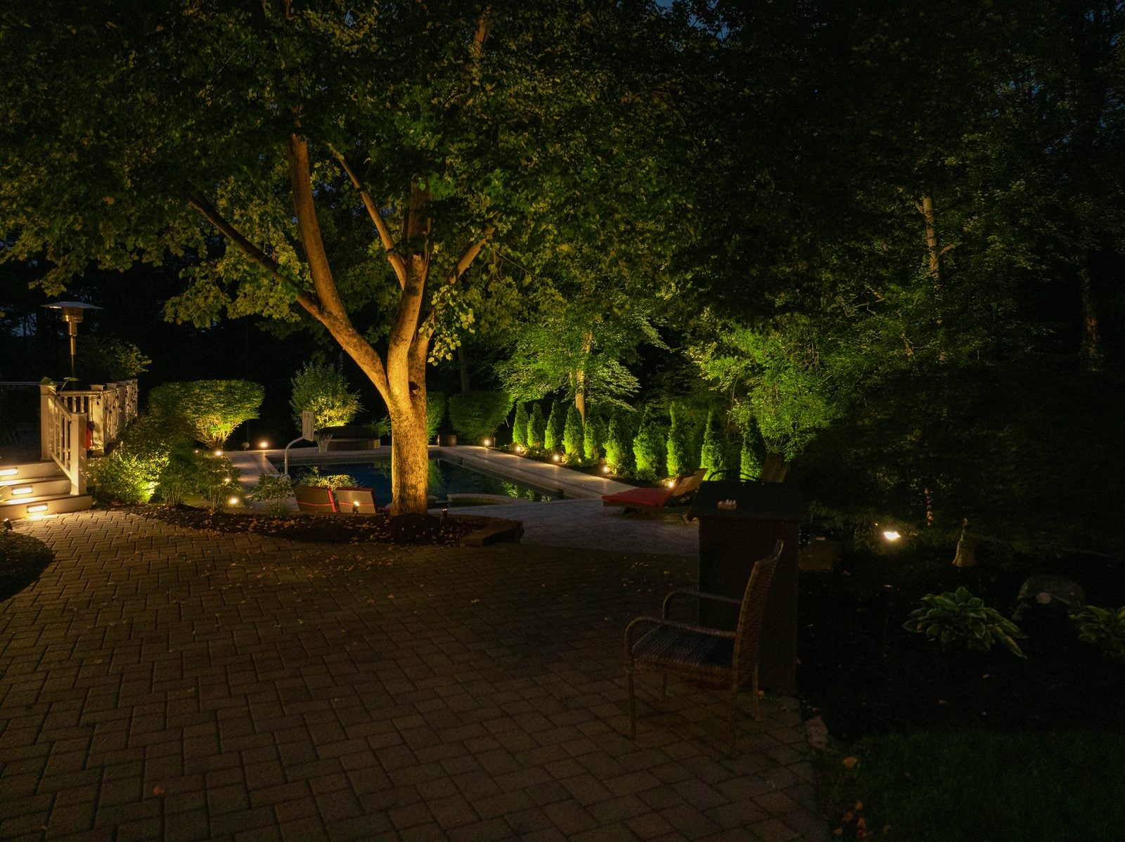 A lit pool at night, the water glowing beneath warm light on the surrounding planting