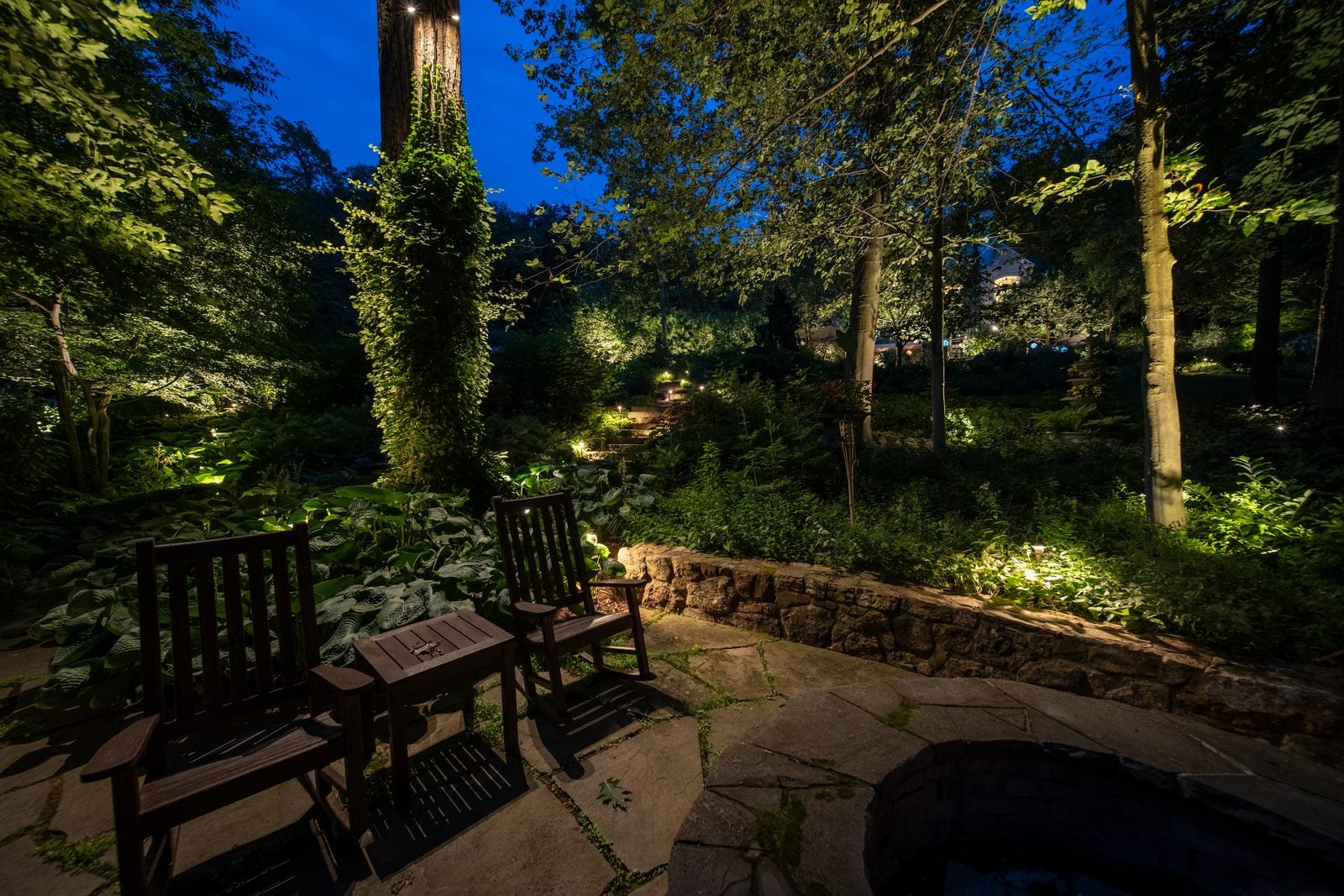 A lit patio and seating area, planting washed behind the furniture