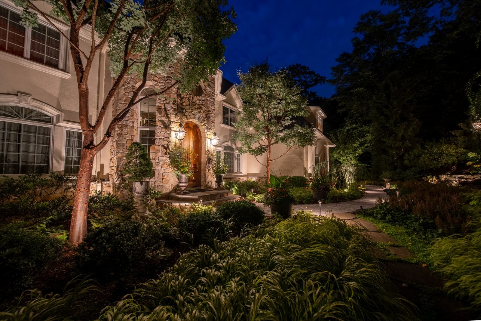 An entry and facade lit from the ground, the drive reading clearly up to the door