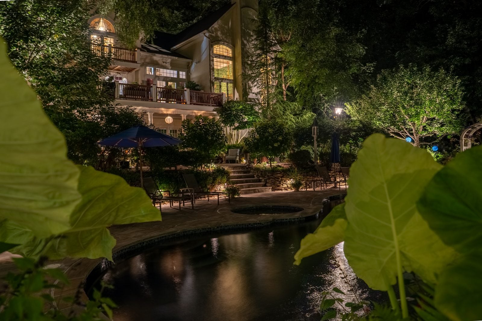A lit pool at night, the water glowing beneath warm light on the surrounding planting