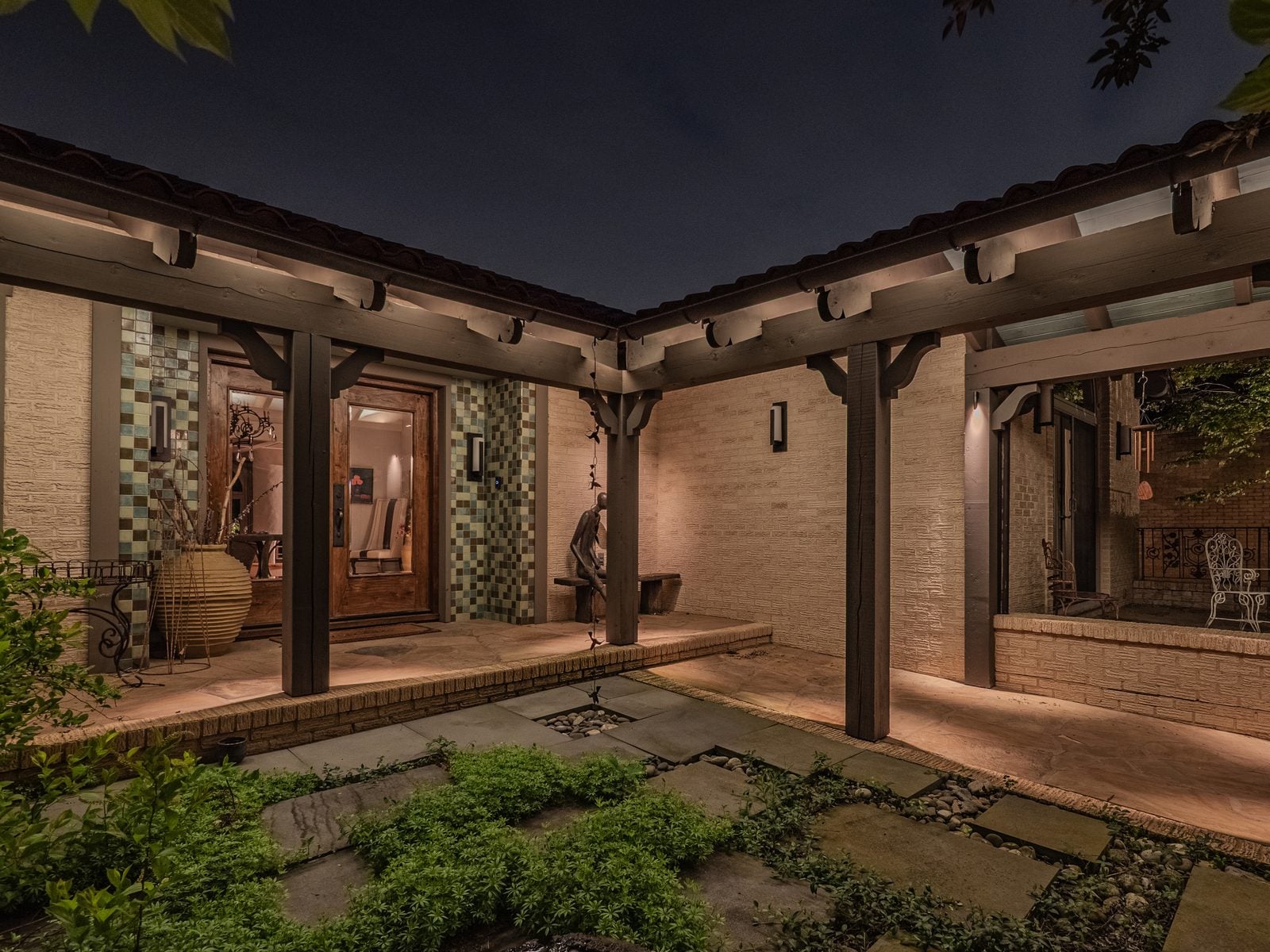 A covered terrace lit warm, the garden beyond uplit
